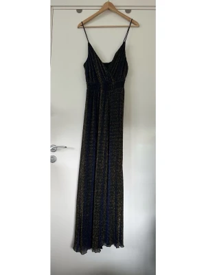 Bik Bok - glittrig byxdress med smala band - storlek XS / S - Festlig lång svart blå guldig byxdress / jumpsuit från BIK BOK i storlek XS (men är elastisk så passar även S). Stilren modell med smala axelband, V-ringning och vida ben. Markerad midja för bästa passform och diskret dragkedja baktill. Fodrad med superfint glittrigt material i svart, blått och guld. Mycket fint skick!