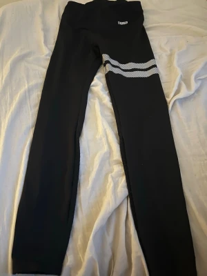 Svarta tights med vita ränder - Snygga svarta tights med två vita, vågiga ränder på ena benet. Tightsen har hög midja och är tillverkade i ett stretchigt material som passar perfekt för träning eller sport. Enkla att matcha med andra träningskläder och riktigt bekväma.