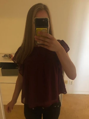Vinröd volangblus med kort ärm - Söt vinröd blus med volangdetaljer och rund hals. Blusen har korta ärmar och är gjord i ett tunt, luftigt material som ger ett flowy intryck.😍