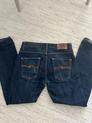 Nudie Jeans dry selvedge - Säljer ett par mörkblå jeans från Nudie Jeans med klassisk femficksmodell och kontrastsömmar i orange. Modellen är grim tim och de är i storlek W29/L30. De är i materialet dry selvedge och har en fin wash. Hör av dig vid frågor elr liknande!