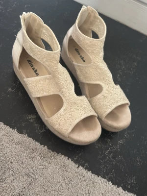 Beige sandaler med platåsula från Din Sko - Säljer ett par beige sandaler från Din Sko med platåsula och öppen tå. Sandalerna har grova remmar i textil med struktur och dragkedja bak för enkel på- och avtagning. Snyggt och trendigt val till sommaren.
