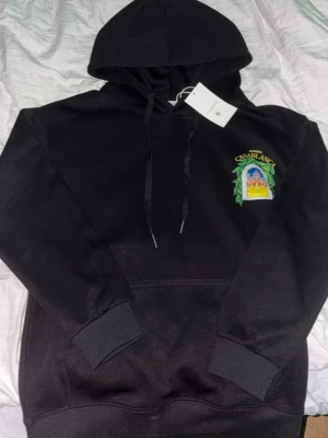 Svart hoodie från Casablanca - Snygg svart hoodie från Casablanca (lapp fof på) med färgglad broderad logga och motiv på bröstet. Klassisk känguruficka framtill, ribbade muddar och justerbar huva med snören. Perfekt för dig som vill ha en stilren men ändå unik hoodie.