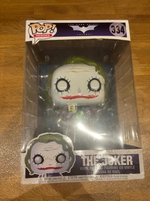 Funko Pop The Joker Dark Knight - Säljer en Funko Pop vinylfigur av The Joker från The Dark Knight-trilogin. Figuren har grönt hår, vitmålat ansikte med röda läppar och mörka ögon. Levereras i originalförpackning med fönster. Perfekt för samlare eller Batman-fans.