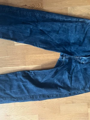 Mörkblå raka jeans - Säljer ett par mörkblå jeans med rak passform och klassisk femficksdesign. Jeansen har hög midja och är tillverkade i kraftigt denimtyg. Perfekta för dig som gillar en tidlös och avslappnad stil.