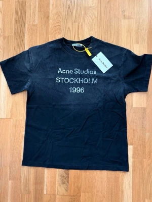 Acne Studios t-shirt - Snygg svart t-shirt från Acne Studios med tryck 'Acne Studios STOCKHOLM 1996' på bröstet. Klassisk passform med rund hals och korta ärmar. Perfekt basplagg med stilren design och diskret logga framtill.