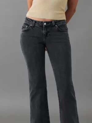 Mörkgrå bootcut jeans med fickdetaljer - Snygga mörkgr bootcut jeans med låg midja och klassiska fem fickor. Baktill finns två fickor med lock och knappdetaljer. Jeansen har en lätt utsvängd passform och är tillverkade i denim med en tvättad look.