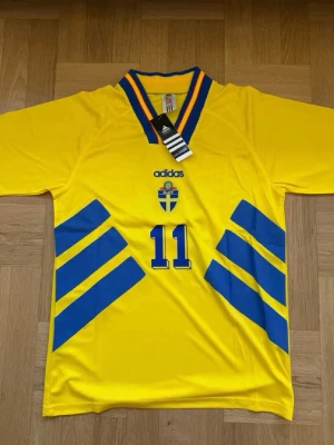 Brolin #11 – Sverige 1994 Hemma (storlek M) - Brolin #11-tryck. Sverige 1994 Borta (vit). Storlek M. Helt ny och aldrig använd. Skickas snabbt 🚚💨  Mått (M): Halvt bröstmått 53 cm • Längd 74 cm • Ärmbredd 23 cm • Axelbredd 44 cm • Ärmlängd 40 cm • Manschett 19 cm.  🔥 Fan Edition – normal passform. 🇸🇪 Sverige landslag.  📩 Skicka gärna ett meddelande vid frågor eller prisförslag! 🛍 Bundle-rabatt upp till 20%! 📦 Skickas samma eller nästa dag.