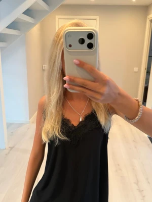 Svart linne med spetsdetaljer - Säljer ett så fint svart linne med tunna axelband och v-ringning. Toppen har fina spetsdetaljer längs urringningen som ger en elegant touch. Perfekt att styla med jeans eller kjol för en trendig look.