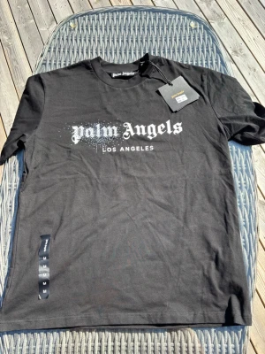 Svart Palm Angels t-shirt M - Säljer en svart t-shirt från Palm Angels med vit logga och texten 'Los Angeles' framtill. T-shirten har klassisk passform, rund halsringning och är kortärmad. Materialet är mjuk bomull och trycket har en cool prickig effekt vid loggan.