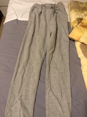 Grå mjukisbyxor med resårmidja - Säljer ett par klassiska grå mjukisbyxor med resår i midjan och benslut. Byxorna är raka i modellen och gjorda i mjukt sweatshirtmaterial, perfekta för chill dagar hemma eller när du vill vara bekväm. Inga synliga loggor eller detaljer.