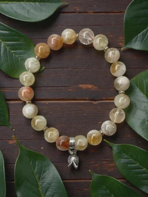 Pärlarmband med silverberlock - Snyggt armband med stora, runda pärlor i jordnära toner av beige, brunt och gult. Armbandet har en silverfärgad berlock i form av en hand. Perfekt accessoar för dig som gillar naturliga material och unika detaljer. Armbandet är elastiskt och pärlorna är citrin kristaller. 