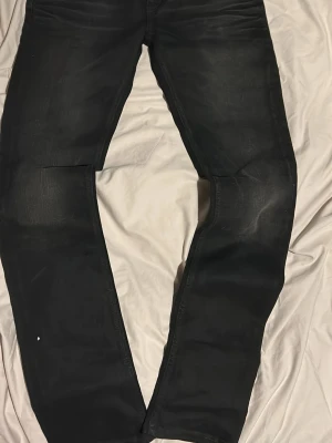 Svarta slim fit jeans - Säljer ett par svarta slim fit jeans med lätt slitna detaljer på låren och knäna. Jeansen har klassisk femficksdesign och raka ben. Perfekta för en stilren och enkel look.kommer med prislappen 