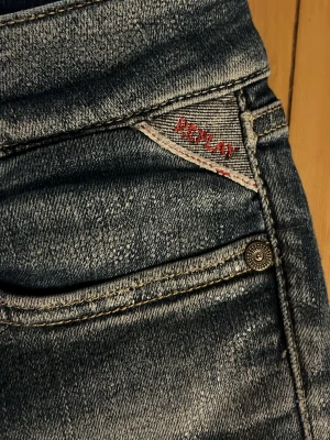 Blå Replay jeans med slitningar - Snygga blå jeans från Replay med coola slitningar och tvättad look. Klassisk femficksmodell med Replay-logga i rött på myntfickan. Jeansen har smal passform och är tillverkade i ett mjukt denimtyg som sitter skönt. W26 L30. Pris kan diskuteras 
