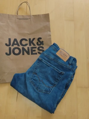 Blå jeans från Jack & Jones - NYA UTAN PRISLAPP!                 Snygga blå jeans från Jack & Jones med klassisk femficksdesign och läderpatch bak i midjan. Jeansen har rak passform och är tillverkade i denim med en autentisk blå tvätt. Perfekta för en avslappnad och trendig stil. En påse från Jack & Jones tillkommer även. Hör av er vid frågor!