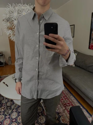 Grå klassisk skjorta, Filippa K - Snygg grå skjorta med diskret rutmönster och klassisk krage. Skjortan har vita knappar framtill och långa ärmar. 