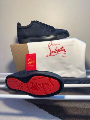 Christian Louboutin Skor - Snygga Mörkblåa sneakers från Christian Louboutin i mocka med klassisk röd sula och diskret logga på sidan. Lågt skaft och Mörkblåa skosnören ger en clean look. Perfekta för dig som vill ha något exklusivt och stilrent i garderoben.
