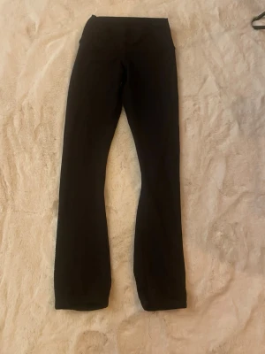 Svarta konståkningsbyxor med diamanter  - Säljer ett par svarta konståkningsbyxor med bootcut-modell och hög midja. De har diskreta detaljer med små blåa prickar längst ner på baksidan av benen. Perfekta för en avslappnad och trendig look.