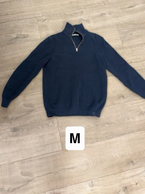 Mörkblå halvzip tröja - Mörkblå stickad tröja med halvzip och hög krage. Tröjan har ribbade muddar vid ärmslut och nederkant, samt en stilren och enkel design som passar till många olika outfits.