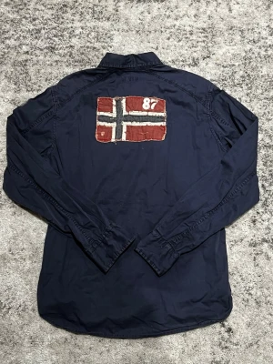 Napajiri Overshirt - En riktigt fin overshirt / skjorta ifrån Napajiri! Den är i storlek M och i ett rätt bra skick! Den har en stor borgerliga på ryggen samt ett emblem på ärmen och en liten Norge-flagga på en av bröstfickorna! 👌 Tveka inte på att skriva ifall du är i behov av fler bilder på plagget eller mått! 📸📏 Skriv vid minsta lilla fundering då jag oftast svarar fort! 💬 Fraktar alltid samma dag eller dagen efter beställning! 🚛 