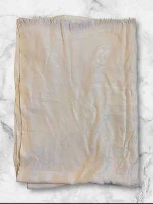 Beige halsduk med logomönster - Snygg beige halsduk i ett glansigt material med diskret invävt logomönster. Halsduken har fransad kant upptill och känns riktigt lyxig och stilren. Perfekt accessoar för att lyfta din outfit med en elegant touch.