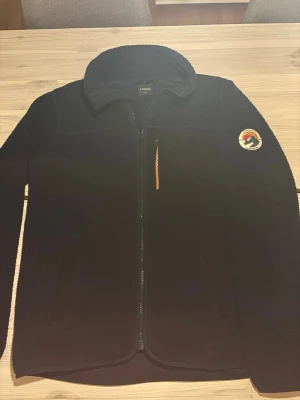 Mörkblå fleecejacka från Everest - Mysig mörkblå fleecejacka från Everest med hel dragkedja, hög krage och bröstficka med orange dragkedja. Patch med Everest-logga på ärmen och två sidofickor. Perfekt för lager-på-lager och outdoor och även perfekt att ha som tröja inomhus men även som vår jacka utomhus! Pris går att diskutera vid snabb affär! Hör gärna av er!