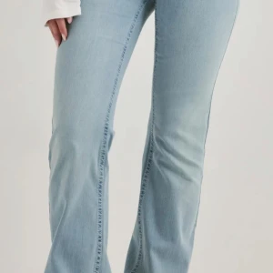 Ljusblå bootcut jeans med brodyr - Säljer ett par ljusblå bootcut jeans med broderade detaljer i rosa på bakfickorna. Jeansen har klassisk femficksdesign och är tillverkade i mjukt denimtyg. Perfekta för en avslappnad och trendig look.