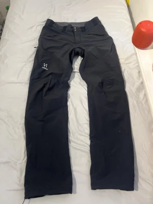 Svarta cargobyxor från Haglöfs - Säljer ett par svarta cargobyxor från Haglöfs med raka ben och dubbla knappar i midjan. Byxorna har diskreta fickor och är tillverkade i ett slitstarkt funktionsmaterial, perfekta för dig som gillar outdoor och streetwear.