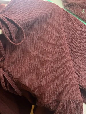 Vinröd blus med knyt - Supersöt vinröd blus från H&M med strukturerat tyg och två knytband framtill. Blusen har trekvartsärm och en avslappnad, flowy passform. Perfekt att styla med jeans eller kjol för en trendig look. Pris kan diskuteras vid snabb affär💗