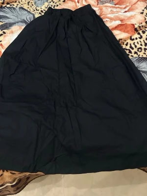 Svart långkjol med resårmidja - En enkel och stilren svart långkjol med resår i midjan. Kjolen har en rak passform och är tillverkad i ett mjukt tyg som faller snyggt. Perfekt att matcha med en crop top eller stickad tröja för en trendig look. Kjolen är i linnematerial och behöver därför strykas. Helt oanvänd. 