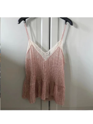 trendig zara topp - Söt rosa linnetopp med tunna axelband och v-ringning dekorerad med vit spets. Toppen har en lätt volang nedtill och är gjord i ett tunt, plisserat material som ger en luftig känsla. Perfekt för varma dagar och enkel att styla.