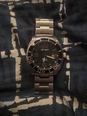 Jet Set Miami herrklocka i silver - Stilren herrklocka från Jet Set, modell Miami, med svart urtavla och tydliga siffror. Klockan har datumvisning och en robust länk i silverfärgat metall. Perfekt accessoar för dig som gillar klassisk och sportig stil.