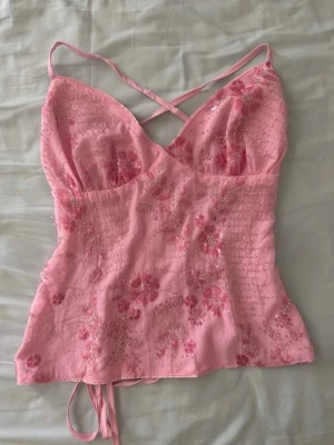 Rosa Y2K topp med pärlor & broderi Ibiza stil  - Superfin rosa Y2K-topp med blombroderier och små pärldetaljer ✨ Sitter jättefint på med figurnära passform och tunna band.  Ger riktig Ibiza / beach club / sommarkväll-känsla 🌴 Perfekt till semester, festival, utekväll eller middagar i solnedgången. Så snygg med linnebyxor, lågmidjade jeans eller en söt kjol.  • Skick: mycket bra • Storlek: XS–S • Färg: rosa • Stil: Y2K / Ibiza / coquette  #y2k #ibizastil #sommartopp #rosatopp #utekväll #festivaloutfit #beachclub #trendigt #2000tal #pärldetaljer
