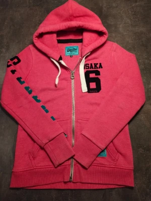 Superdry zip hoodie - Fin rosa röd superdry zip hoodie i väldigt bra skick storlek S och de står superdry på högra armen. Damtröja men passar även killar