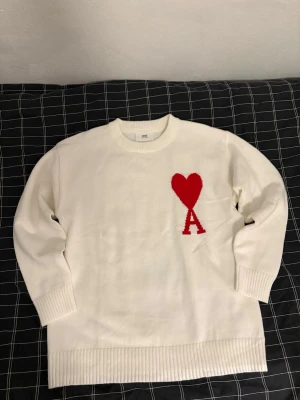 Vit stickad tröja från Ami Paris - Säljer en vit stickad tröja från Ami Paris med röd hjärtdetalj och bokstaven A på bröstet. Tröjan har rund hals, ribbade muddar och lång ärm. Perfekt för dig som vill ha en clean men ändå unik look. Använt en gång, inga defekter, i nyskick. Hör av dig om du har några frågor. Kan gå ner till 400 vid snabb affär behöver få såldt snabbt