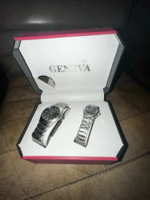 Geneva silverfärgade klockor i set - Säljer ett set med två stilrena klockor från Geneva i silverfärg. Båda har metallarmband och klassisk design, en med svart urtavla och en med silverfärgad urtavla. Kommer i original ask med Geneva-logga. Perfekt för dig som vill matcha accessoarer.