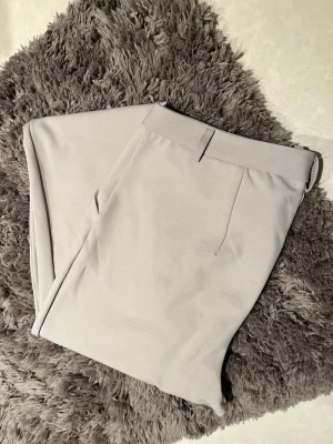 Beige kostymbyxa från lager 157 - Stilrena beige kostymbyxor från lager 157 med raka ben och diskreta sidofickor. Byxorna har en klassisk knappstängning och är tillverkade i ett mjukt, vävt material som ger en clean look. Använd ett fåtal gånger och i väldigt bra skick.
