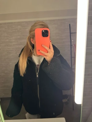 Svart teddyjacka med dragkedja - Mysig svart teddyjacka med dragkedja framtill och hög krage. Jackan har en oversized passform och är tillverkad i fluffigt teddy-material som ger en cool och avslappnad look. Perfekt för kalla dagar när du vill vara både varm och trendig. Storlek S och tycker om den i storleken!❤️