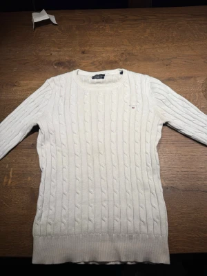 Vit kabelstickad tröja från Gant - Kabelstickad vit tröja från Gant i mjuk bomull. Klassisk rund halsringning och ribbade muddar vid ärmslut. Finns ett litet hål i armen men inget som märks av. Stolek XS men passar även S🙌 Perfekt för en clean och stilren look!