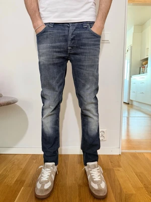Nudie jeans med slitningar - Snygga blå slim fit jeans med slitningar och tvättade detaljer på framsidan och baksidan. Klassisk femficksmodell med normal midja och raka ben. Jeansen har en modern look och passar perfekt till en avslappnad stil.