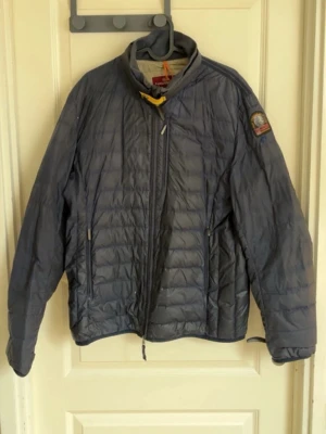 Mörkblå dunjacka från Parajumpers - Snygg mörkblå dunjacka från Parajumpers med gul detalj vid halsen och patch på ärmen. Jackan har två dragkedjeförsedda fickor fram och quiltad design. Perfekt för kalla vinterdagar och har en modern, sportig look.