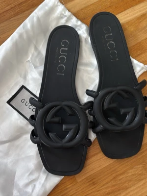 Svarta sandaler exklusiva helt nya bara provade  - Snygga svarta sandaler med stor GG-logga framtill. Tillverkade i gummi med fyrkantig tå och öppen häl. Perfekta för dig som vill ha en trendig och stilren look med lyxig känsla.