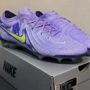 Lila Nike Phantom GX II Elite fotbollsskor - Säljer ett par lila Nike Phantom GX Elite fotbollsskor med neonfärgade detaljer och mönstrad ovandel. Skorna har låg profil, snörning och är tillverkade i ett lätt syntetmaterial för bästa bollkontroll på planen. Perfekta för dig som vill sticka ut på matchen! Storlek 44
