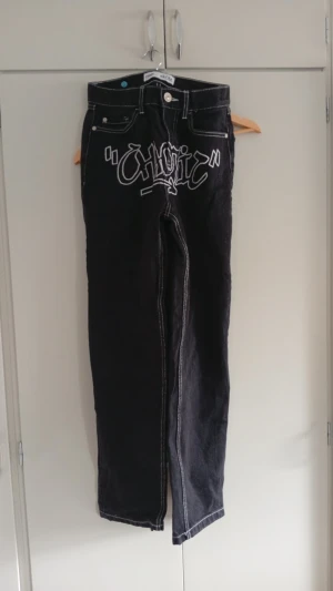 Jeans  - Säljer ett par svarta jeans från FSBN med vit graffiti-inspirerad text på framsidan. Jeansen har raka ben, kontrastsömmar och klassisk femficksmodell. Materialet är denim och de har en cool streetwear-vibe.