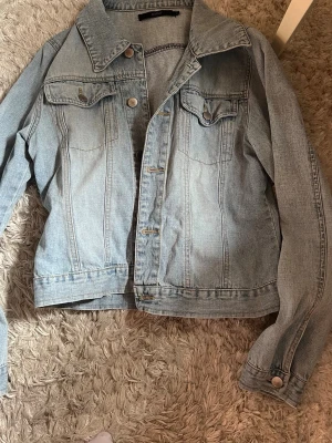 Ljusblå klassisk jeansjacka - Snygg ljusblå jeansjacka i klassisk modell med två bröstfickor med lock och knapp, samt knappstängning framtill. Jackan har raka ärmar och en bred krage. Perfekt att slänga över en hoodie eller t-shirt för en avslappnad look. Det står att storleken är L men det är inte mycket större än S eller XS