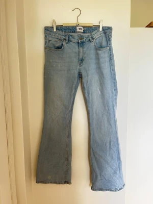 Ljusblå bootcut jeans - Säljer ett par ljusblå bootcut jeans med klassisk design och låg midja. Jeansen har en avslappnad passform och är tillverkade i mjukt denimtyg. Jeansen har små pigmentskiftingar i tyget men inget som syns tydligt.