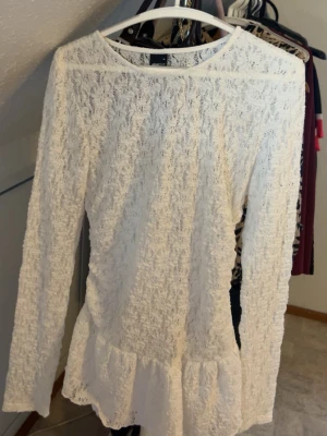Vit spetsblus med volang - Säljer en vit långärmad blus i spets med rund halsringning och volang nedtill. Köpt hos gina ett halvår sen. Använd 2 gånger.