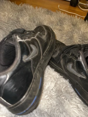 Nike Air Force 1 Low Jewel Black Grey Royal -  ORIGINAL PRIS❌ = 2450kr MIN PRIS 499 ✅ Svarta sneakers med lågt skaft och blå detalj på sulan. Skorna har en klassisk siluett med snörning och en tydlig sula med cirkelmönster undertill. Materialet ser ut att vara syntet eller läderimitation. Perfekta för en streetwear-look. Kan sänka pris vid snabb affär 💨 