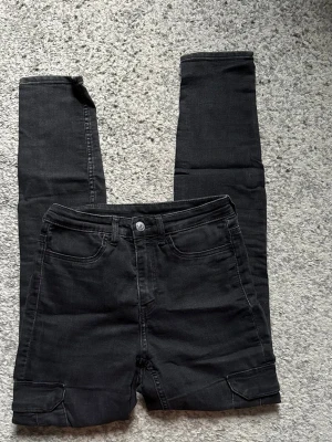 Svarta cargobyxor med fickor - Säljer ett par svarta cargobyxor med raka ben och flera praktiska fickor, både fram och bak samt på benen. Byxorna har knapp och dragkedja i midjan och är tillverkade i ett mjukt, stretchigt material som ger en skön passform.