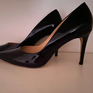 Svarta lackpumps med spetsig tå - Snygga svarta pumps i glansigt lackmaterial med spetsig tå och smal klack. Klassisk och elegant design med beige innersula. Perfekta för dig som vill ha en stilren och trendig look.