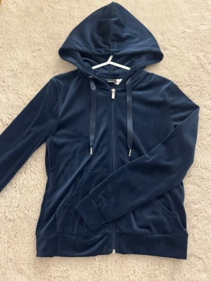 Mörkblå velourhoodie  - Mysig mörkblå hoodie i mjuk velour från Gina Tricot. Dragkedja framtill, huva med dragsko och två fickor. Perfekt för en chill och avslappnad stil. Snygga detaljer med breda muddar och silvriga snörstoppar.